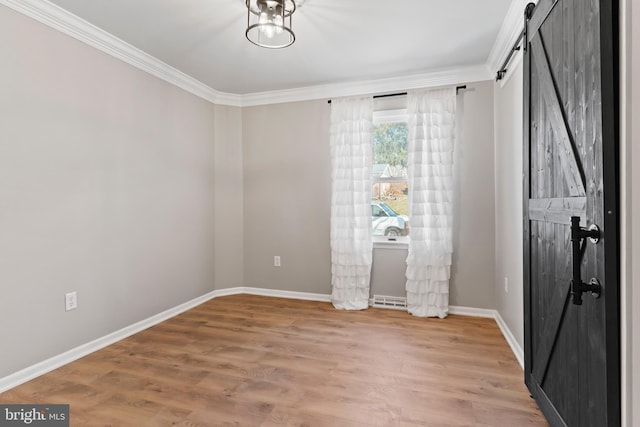 spare room with crown molding, baseboards, light wood-style floors, and a barn door