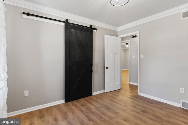 unfurnished bedroom featuring a barn door, wood finished floors, baseboards, and ornamental molding