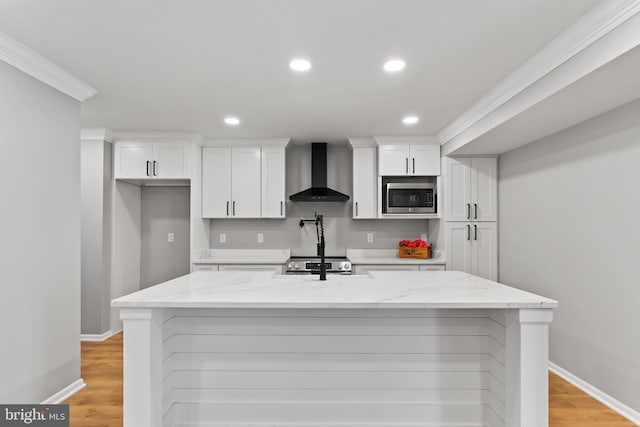 kitchen with wall chimney range hood, a center island with sink, light wood-type flooring, appliances with stainless steel finishes, and white cabinets