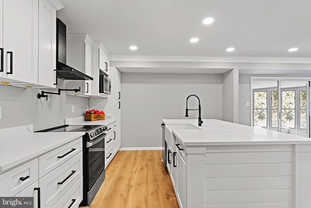 kitchen with a center island with sink, light countertops, appliances with stainless steel finishes, white cabinets, and wall chimney exhaust hood