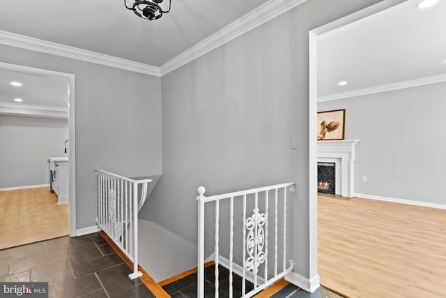 staircase with crown molding, baseboards, recessed lighting, a warm lit fireplace, and wood finished floors