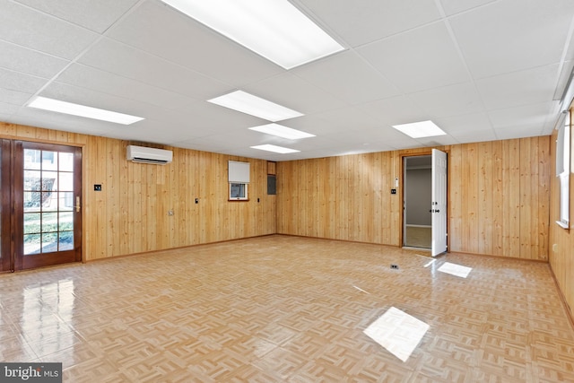 unfurnished room with a wall mounted AC, a drop ceiling, wood walls, baseboards, and parquet flooring