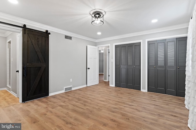 unfurnished bedroom with light wood-type flooring, a barn door, visible vents, and crown molding