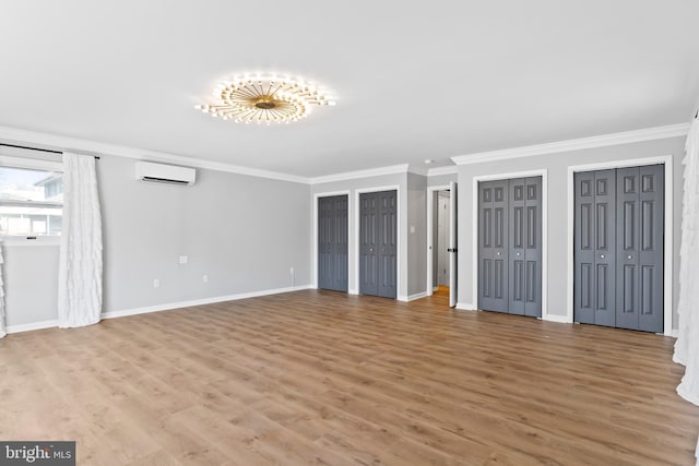 unfurnished living room with a wall mounted air conditioner, baseboards, wood finished floors, and ornamental molding