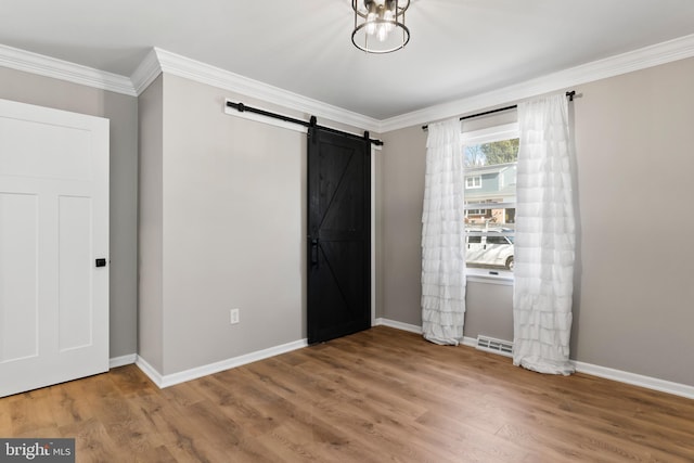 unfurnished bedroom with crown molding, a barn door, wood finished floors, and baseboards