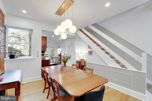 dining room with a chandelier, a decorative wall, stairs, and light wood-style floors