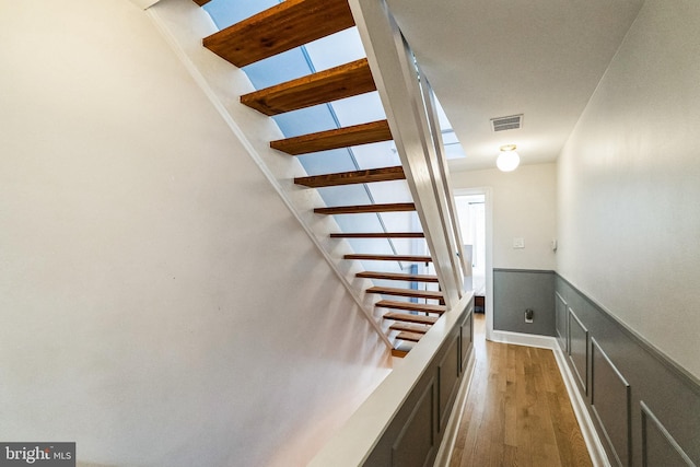 staircase with visible vents, wood finished floors, and wainscoting