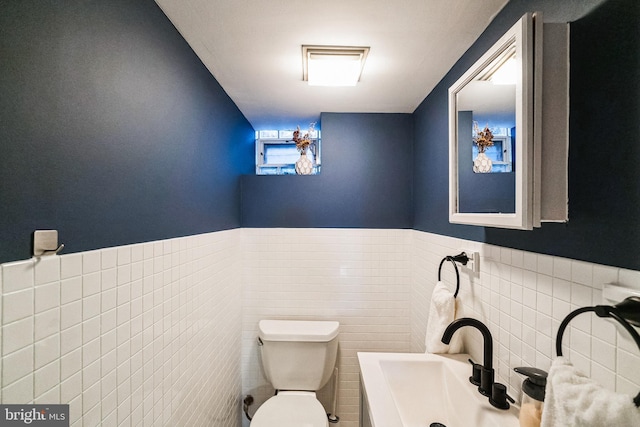 half bathroom with tile walls, toilet, a wainscoted wall, and a sink