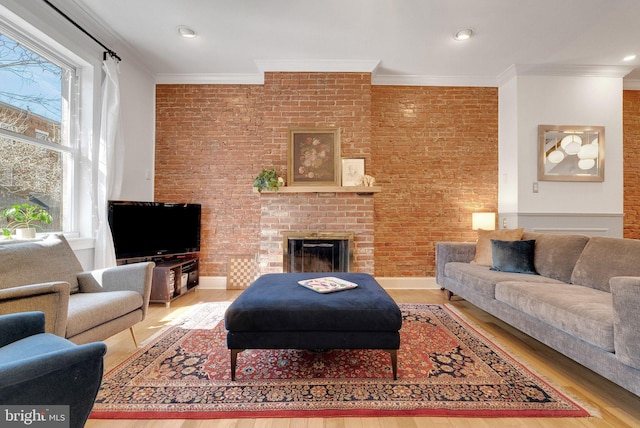 living room featuring a brick fireplace, brick wall, crown molding, and wood finished floors