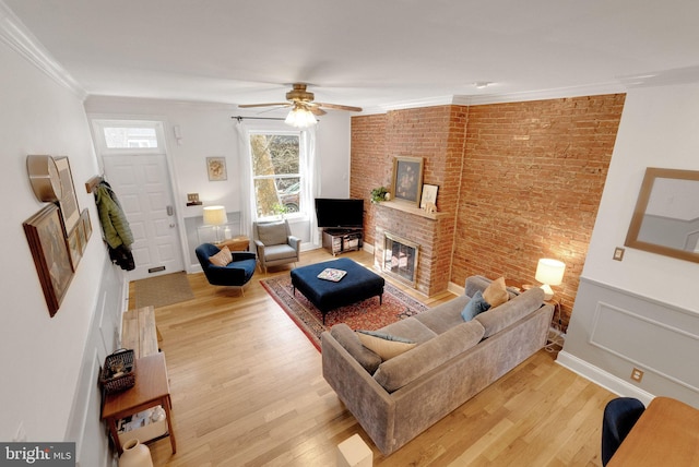 living room with a wainscoted wall, light wood-style flooring, a fireplace, a decorative wall, and crown molding