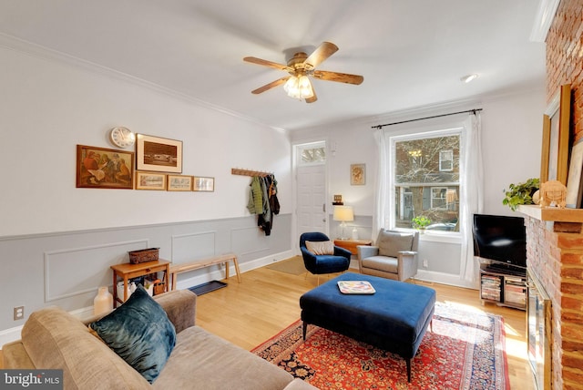 living area with ceiling fan, wood finished floors, ornamental molding, and wainscoting