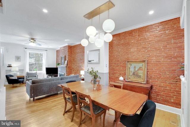 dining room featuring brick wall, baseboards, crown molding, and light wood-style floors