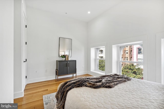 bedroom featuring recessed lighting, a high ceiling, baseboards, and wood finished floors