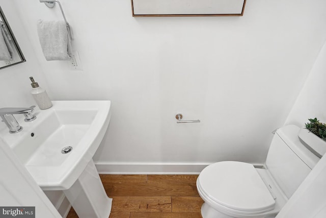 half bathroom featuring a sink, baseboards, toilet, and wood finished floors