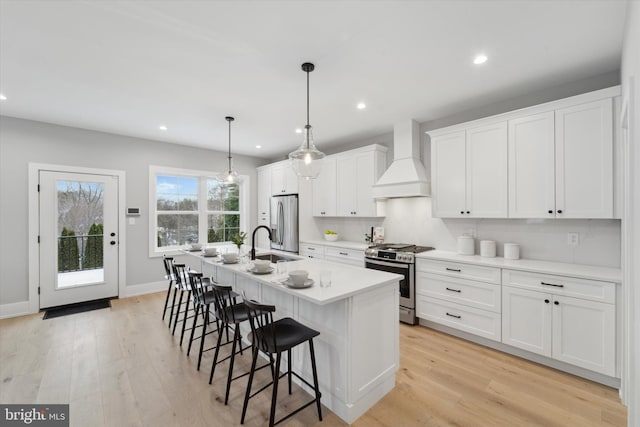 kitchen with light wood finished floors, a kitchen island with sink, stainless steel appliances, custom range hood, and a kitchen breakfast bar