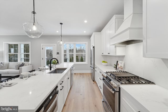 kitchen with premium range hood, a sink, white cabinetry, appliances with stainless steel finishes, and light wood finished floors