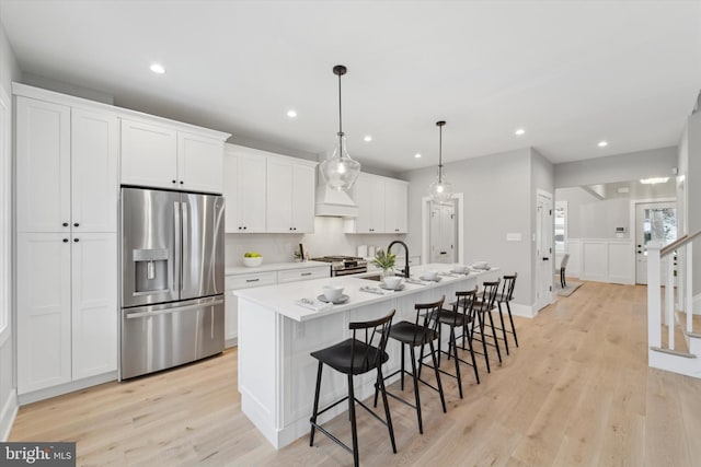 kitchen featuring light wood-style flooring, an island with sink, a sink, stainless steel appliances, and white cabinets