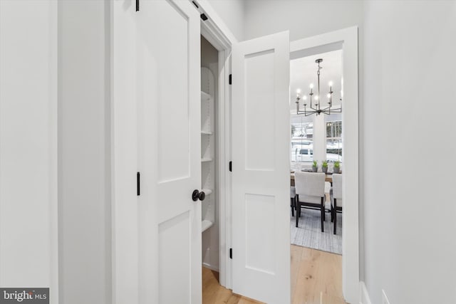 corridor with light wood-style flooring, a barn door, and a chandelier