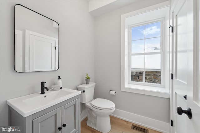 bathroom featuring vanity, wood finished floors, baseboards, visible vents, and toilet