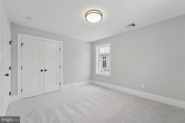 unfurnished bedroom with baseboards, visible vents, a closet, and light carpet