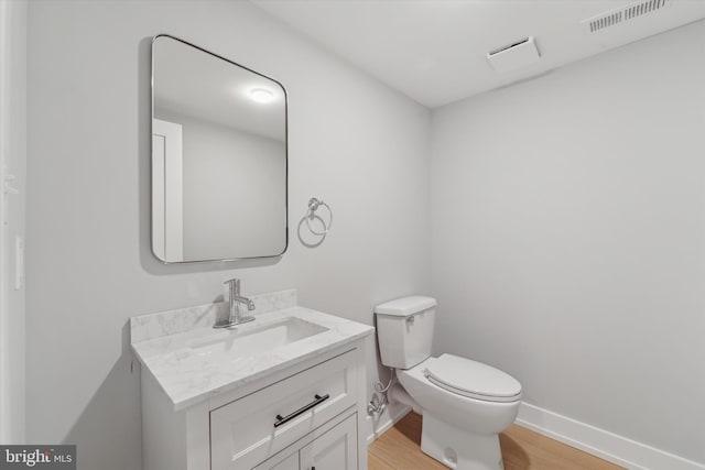 bathroom featuring visible vents, baseboards, toilet, wood finished floors, and vanity