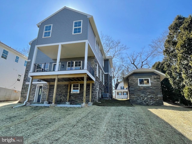 back of property featuring a yard, stone siding, and a balcony