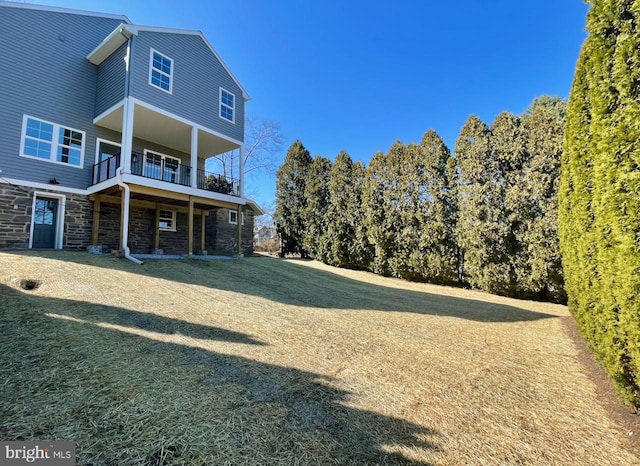 back of house with a balcony, a lawn, and stone siding