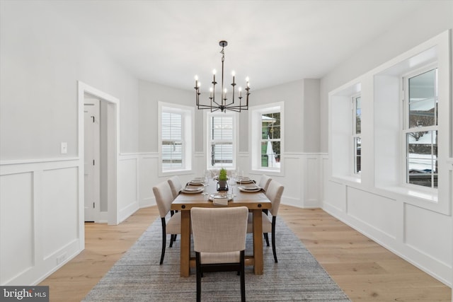 dining room featuring an inviting chandelier, a decorative wall, and light wood-style flooring