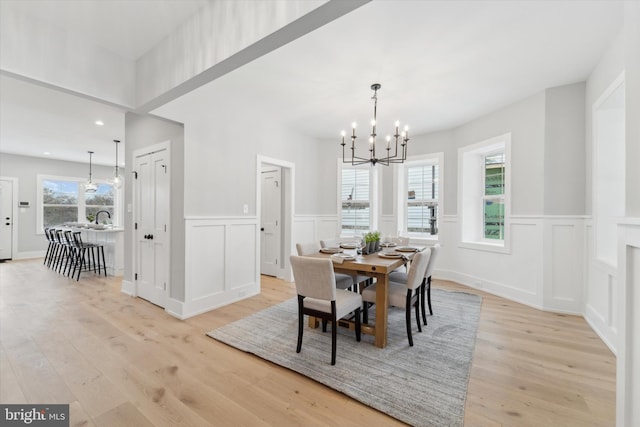 dining area with a decorative wall, a chandelier, wainscoting, and light wood finished floors