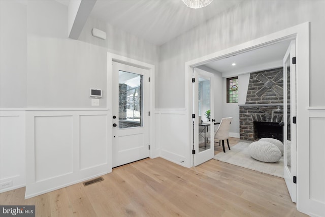 entrance foyer featuring visible vents, light wood-style floors, a stone fireplace, and wainscoting