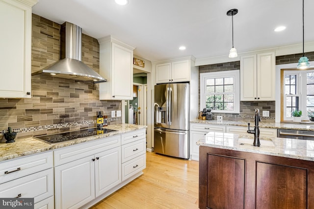 kitchen with a sink, wall chimney range hood, plenty of natural light, and stainless steel appliances