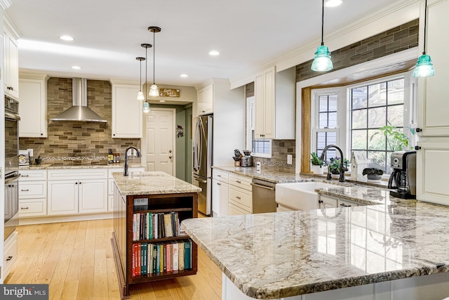 kitchen featuring a sink, stainless steel appliances, wall chimney exhaust hood, light wood finished floors, and light stone countertops