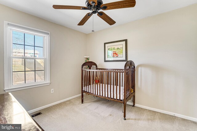 bedroom featuring visible vents, a ceiling fan, a nursery area, baseboards, and light colored carpet