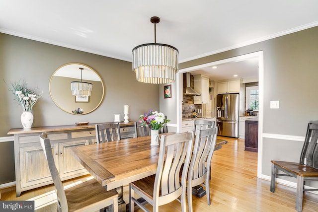 dining space with light wood-type flooring, baseboards, a notable chandelier, and ornamental molding