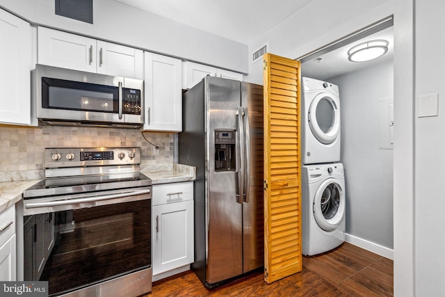 kitchen featuring visible vents, stainless steel appliances, stacked washer / drying machine, white cabinetry, and backsplash