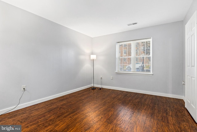 empty room featuring dark wood finished floors, visible vents, and baseboards