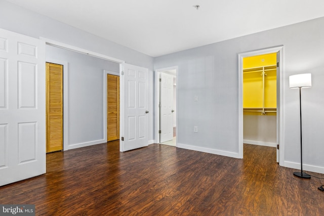 unfurnished bedroom with a spacious closet, wood finished floors, baseboards, and a closet