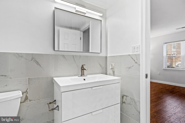 half bathroom with vanity, wood finished floors, visible vents, tile walls, and toilet