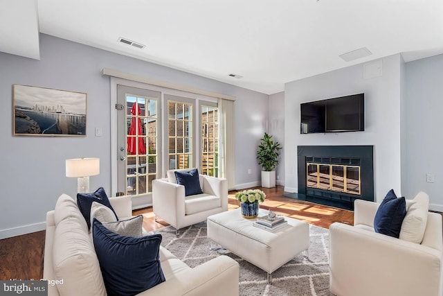 living area with visible vents, a fireplace with flush hearth, baseboards, and wood finished floors