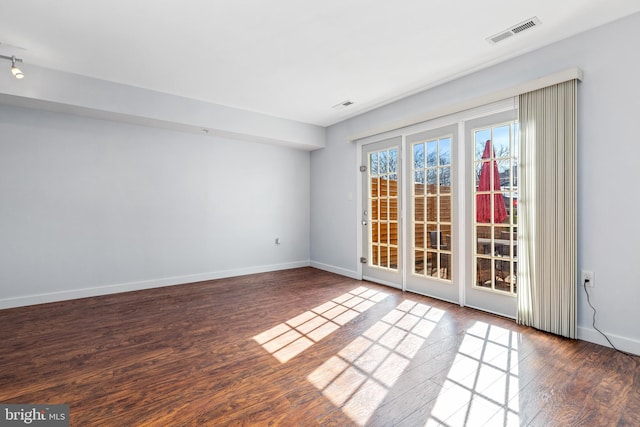 spare room with wood finished floors, visible vents, and baseboards