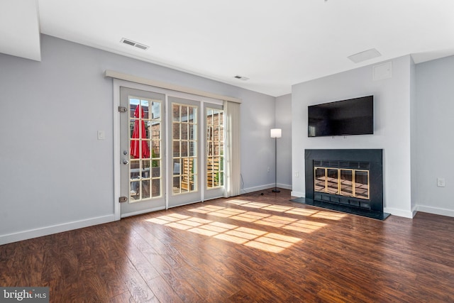 unfurnished living room featuring hardwood / wood-style floors, visible vents, baseboards, and a glass covered fireplace