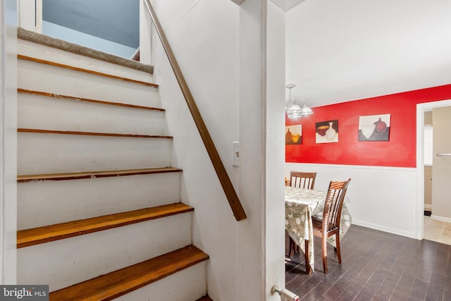 stairway featuring baseboards, an inviting chandelier, and wood finished floors