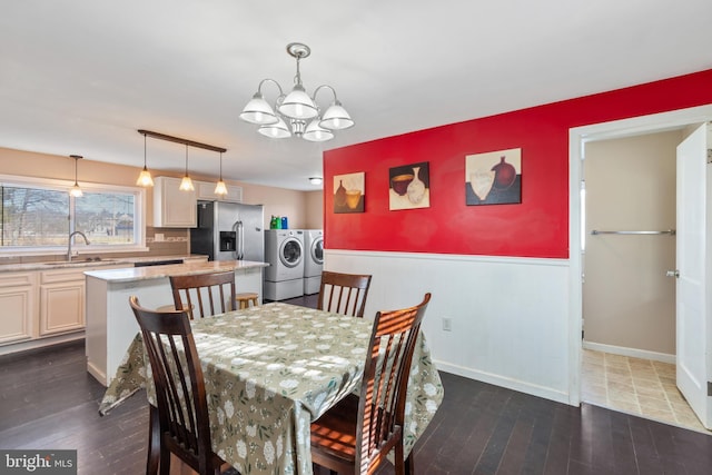 dining room featuring dark wood finished floors, a wainscoted wall, washing machine and dryer, and an inviting chandelier