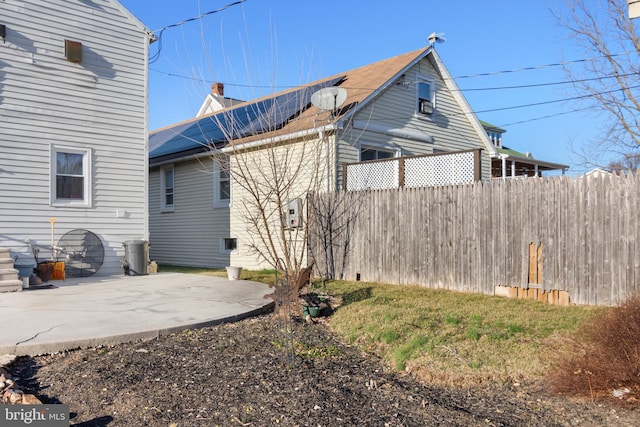 rear view of house with solar panels, a patio, and fence