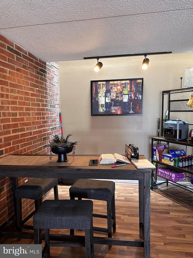 dining room featuring a textured ceiling, wood finished floors, brick wall, and a bar