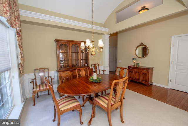 dining room with a wainscoted wall, a notable chandelier, wood finished floors, lofted ceiling, and ornate columns