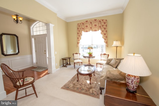 sitting room featuring an inviting chandelier, wainscoting, a decorative wall, crown molding, and ornate columns