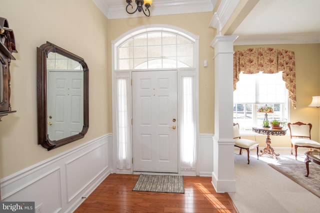 foyer entrance featuring light wood-type flooring, plenty of natural light, crown molding, and ornate columns