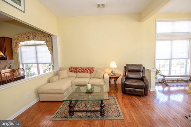 living area with beamed ceiling, baseboards, visible vents, and wood-type flooring