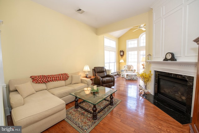 living area featuring visible vents, lofted ceiling, a high end fireplace, ceiling fan, and hardwood / wood-style flooring